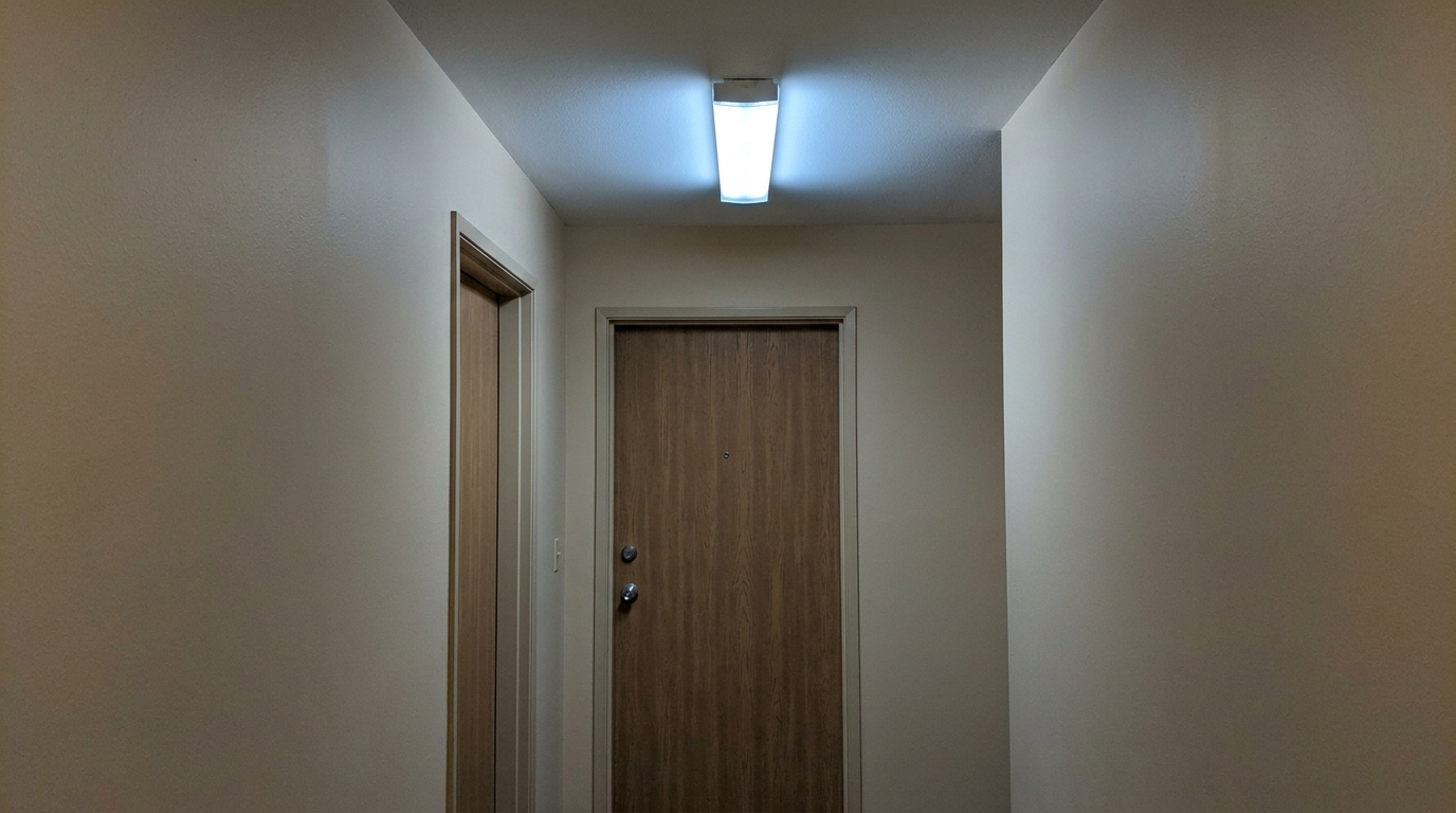 Apartment door lit only by a distant shared corridor ceiling light, no dedicated fixture nearby.