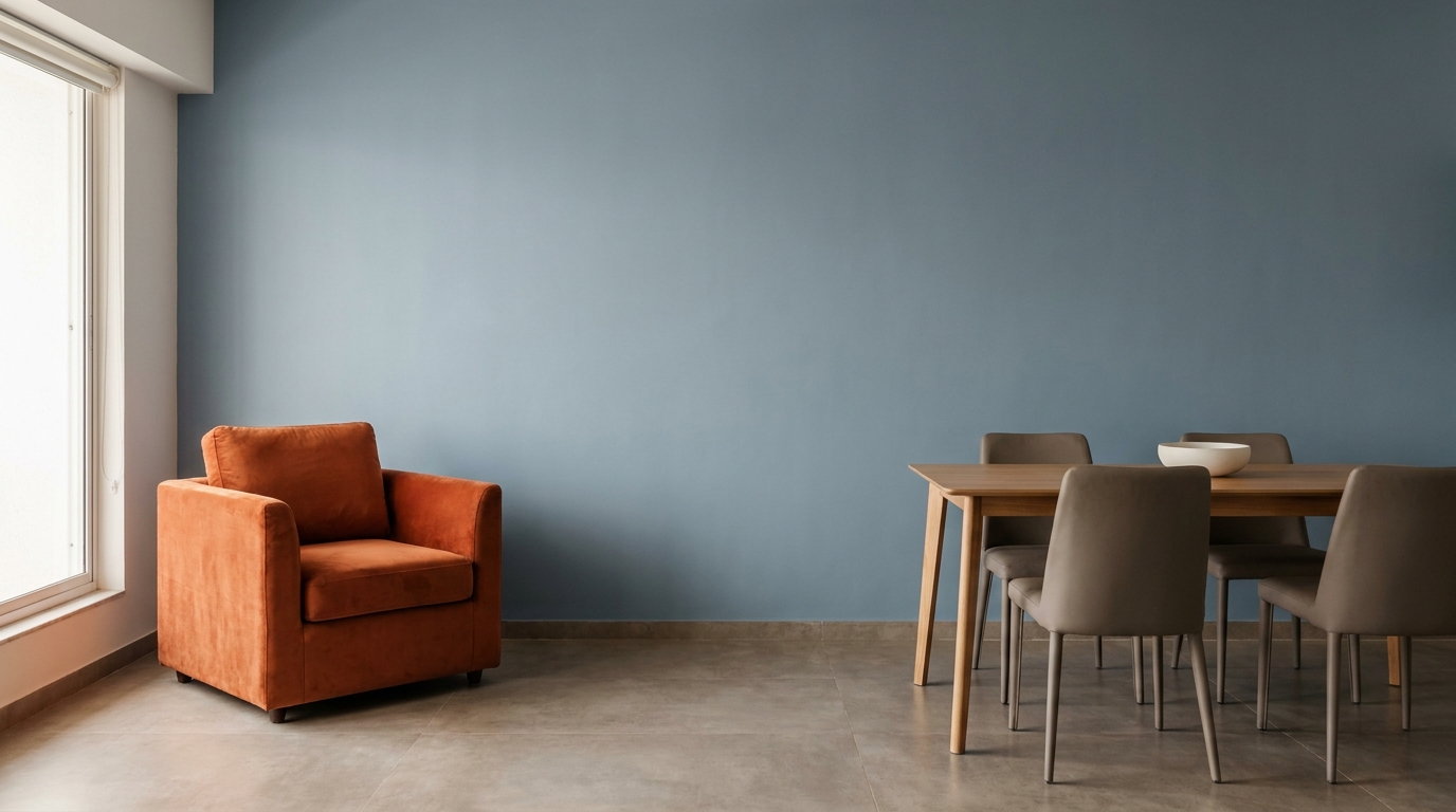 Modern Indian living-dining space with a full matte slate blue wall, a single burnt orange velvet armchair, and warm grey concrete-look flooring
