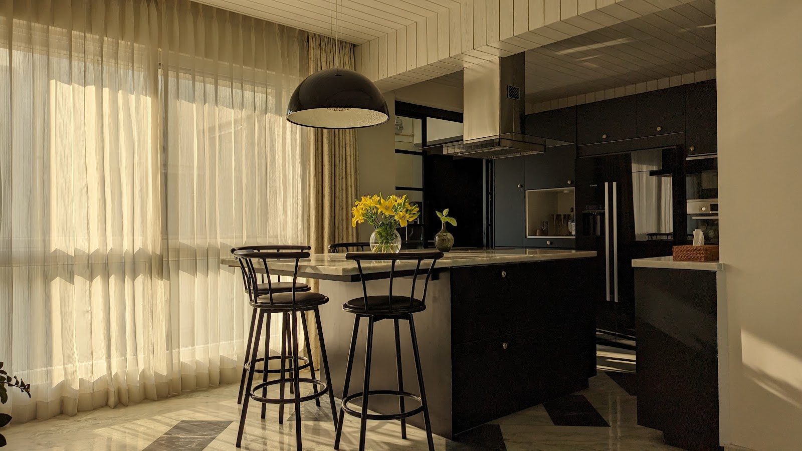 Kitchen island in matte black cabinetry with a white marble countertop and a black dome pendant light, bar stools alongside