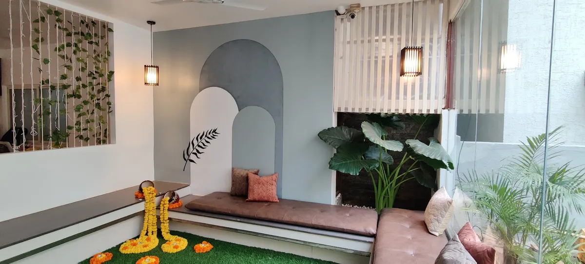 Home entrance nook with a dusty-blue arch wall mural, a built-in cushioned bench, marigold-garlanded slippers on artificial turf, and a live plant wall.