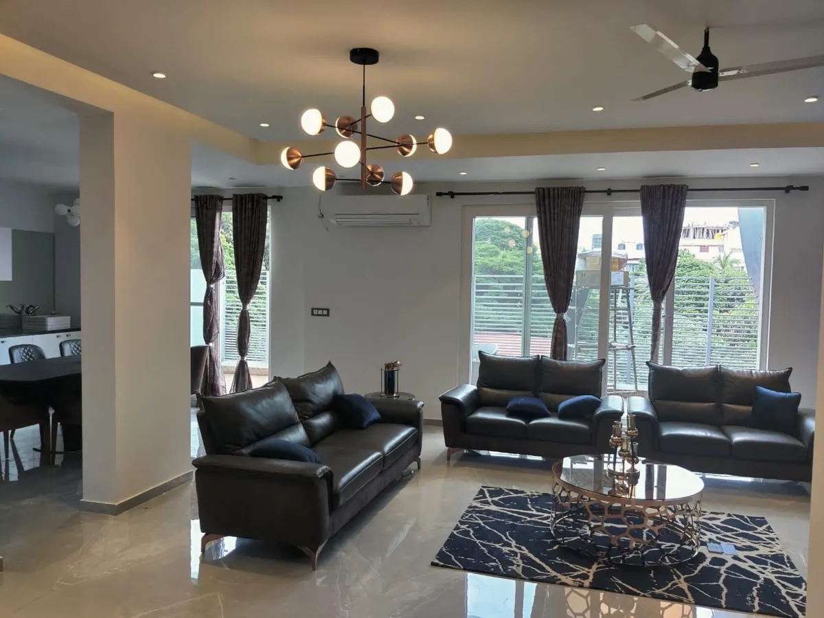 Large daylit living room with three dark leather sofas around an oval mirror-top coffee table on a black-and-gold marbled rug