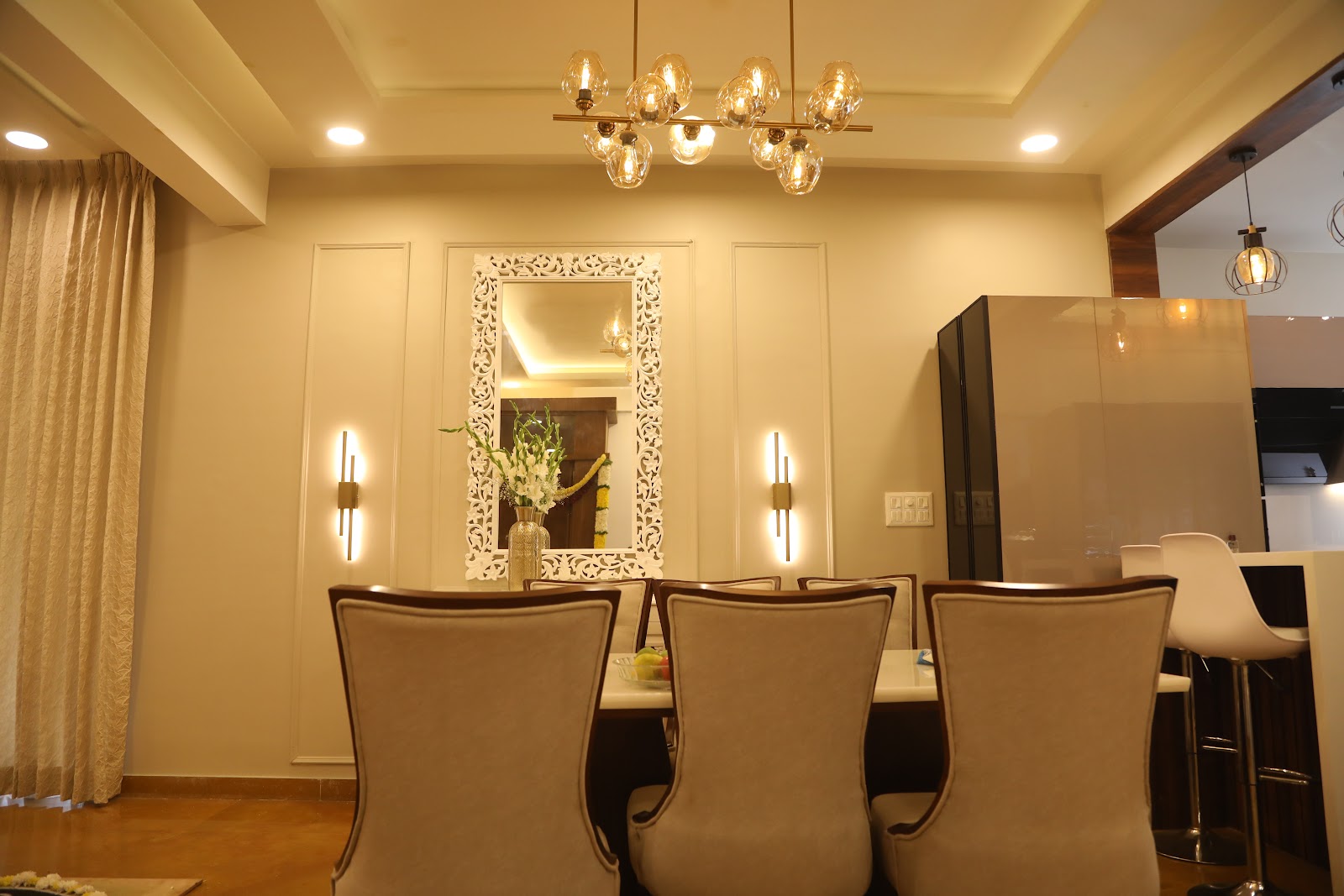 Dining area with a carved white-frame mirror flanked by wall sconces, wood floor, and a smoked-glass cabinet opening to the kitchen.