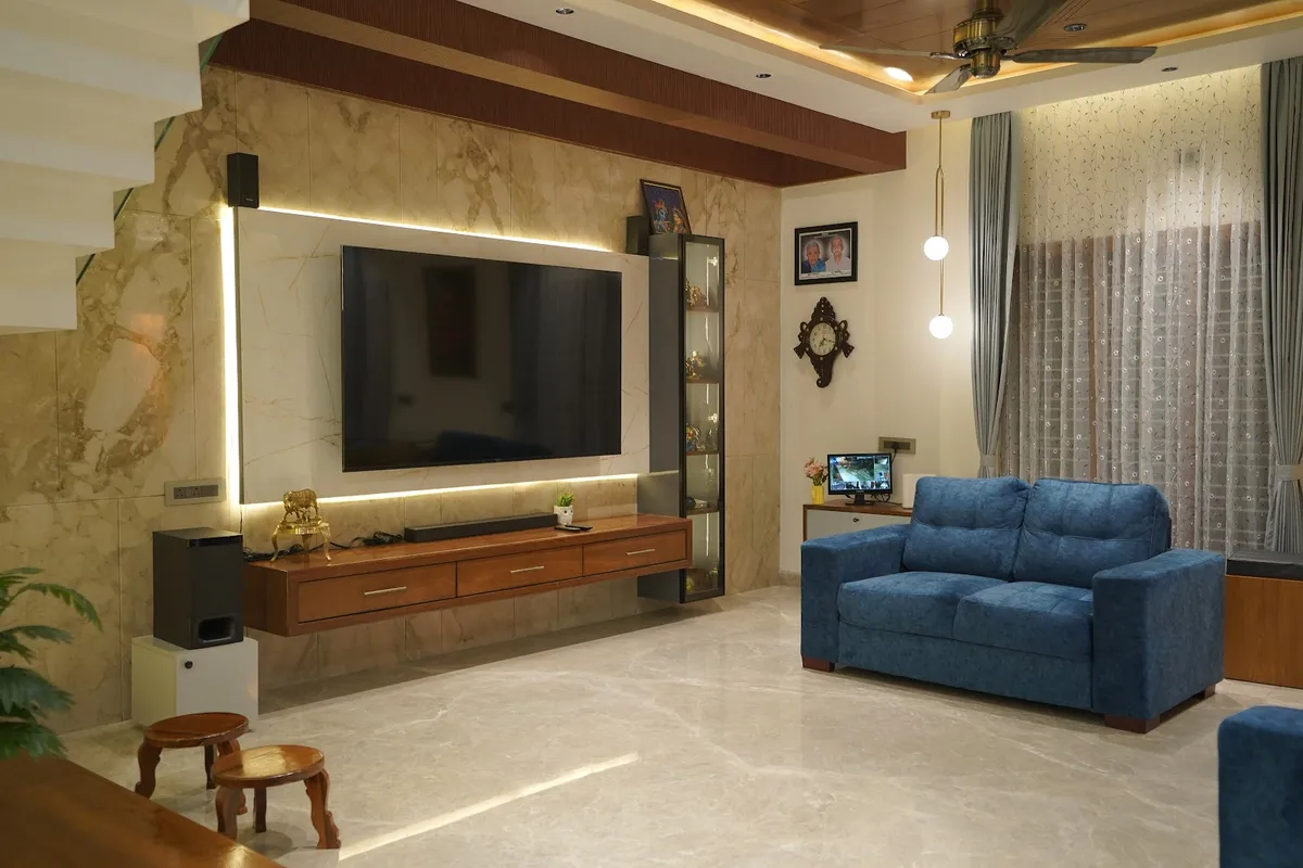 Beige marble-clad TV wall with a backlit LED reveal around the screen, a floating teak drawer console and a slim glass display column