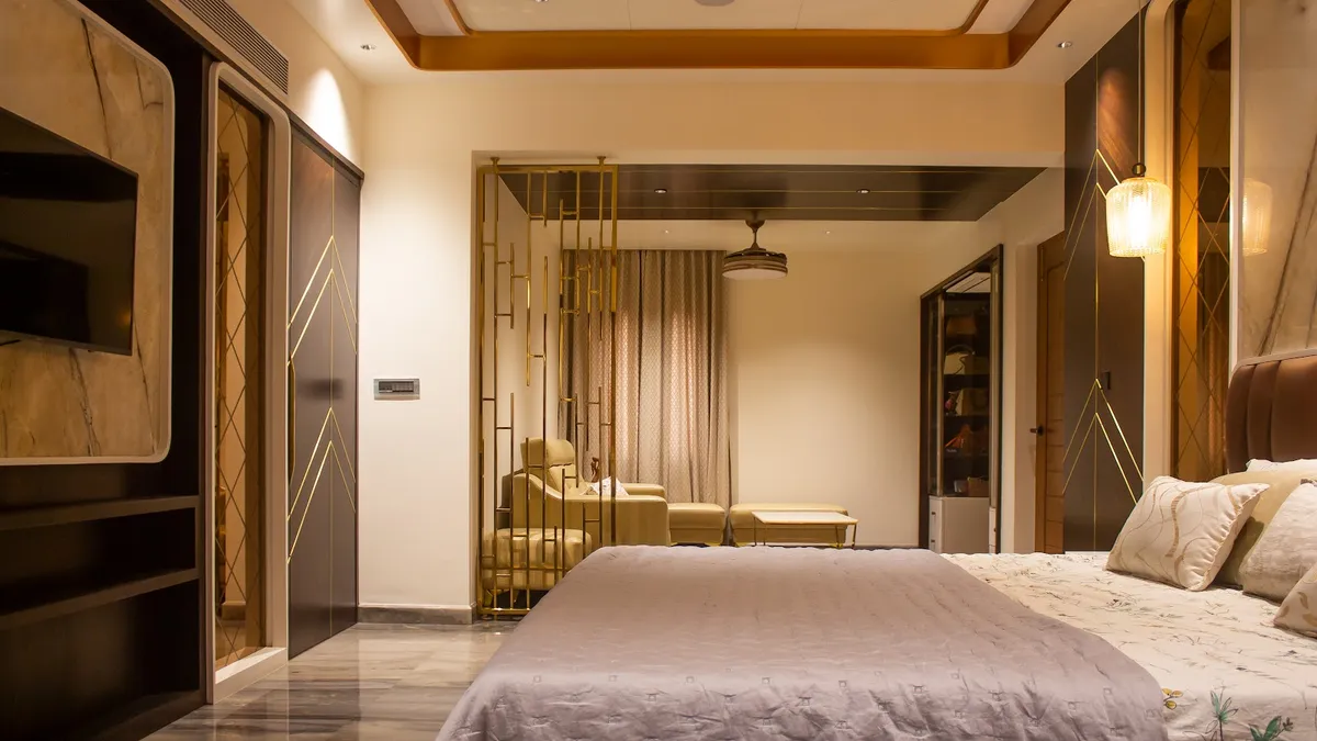 Master bedroom shot from the foot of the bed through a floor-to-ceiling brass fin screen into an attached sitting alcove with two tub chairs