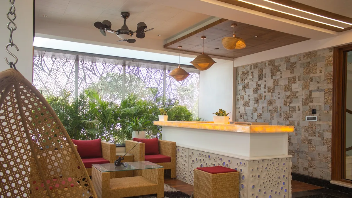 Covered balcony lounge with a hanging rattan swing chair, wicker armchairs in red cushions, a backlit onyx bar counter, and a mother-of-pearl mosaic wall.
