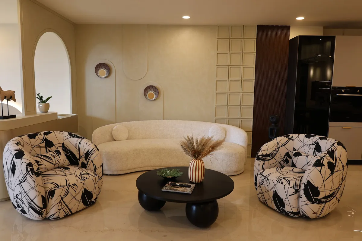 Living room with a curved cream boucle sofa flanked by black-and-white graphic-print swivel armchairs, a round black pedestal coffee table