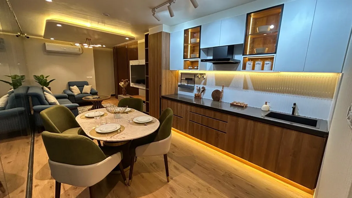Compact open-plan flat where a straight-line kitchen in walnut base units and powder-blue matt wall cabinets faces a round marble-top dining table with olive