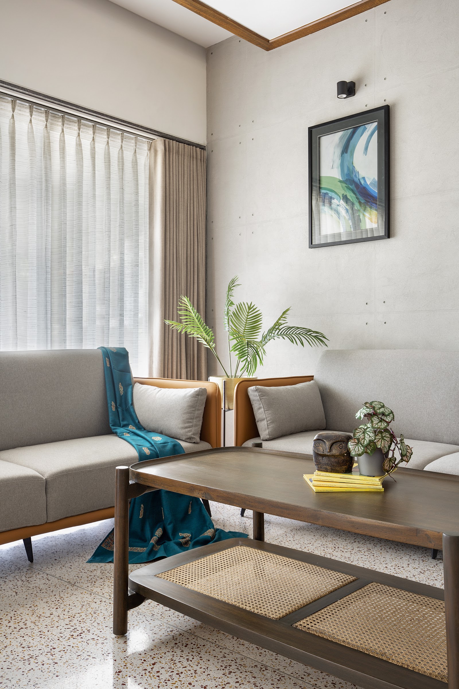 Living room with board-formed concrete walls, a terrazzo floor, and mid-century-style grey sofas around a wood-and-cane coffee table.