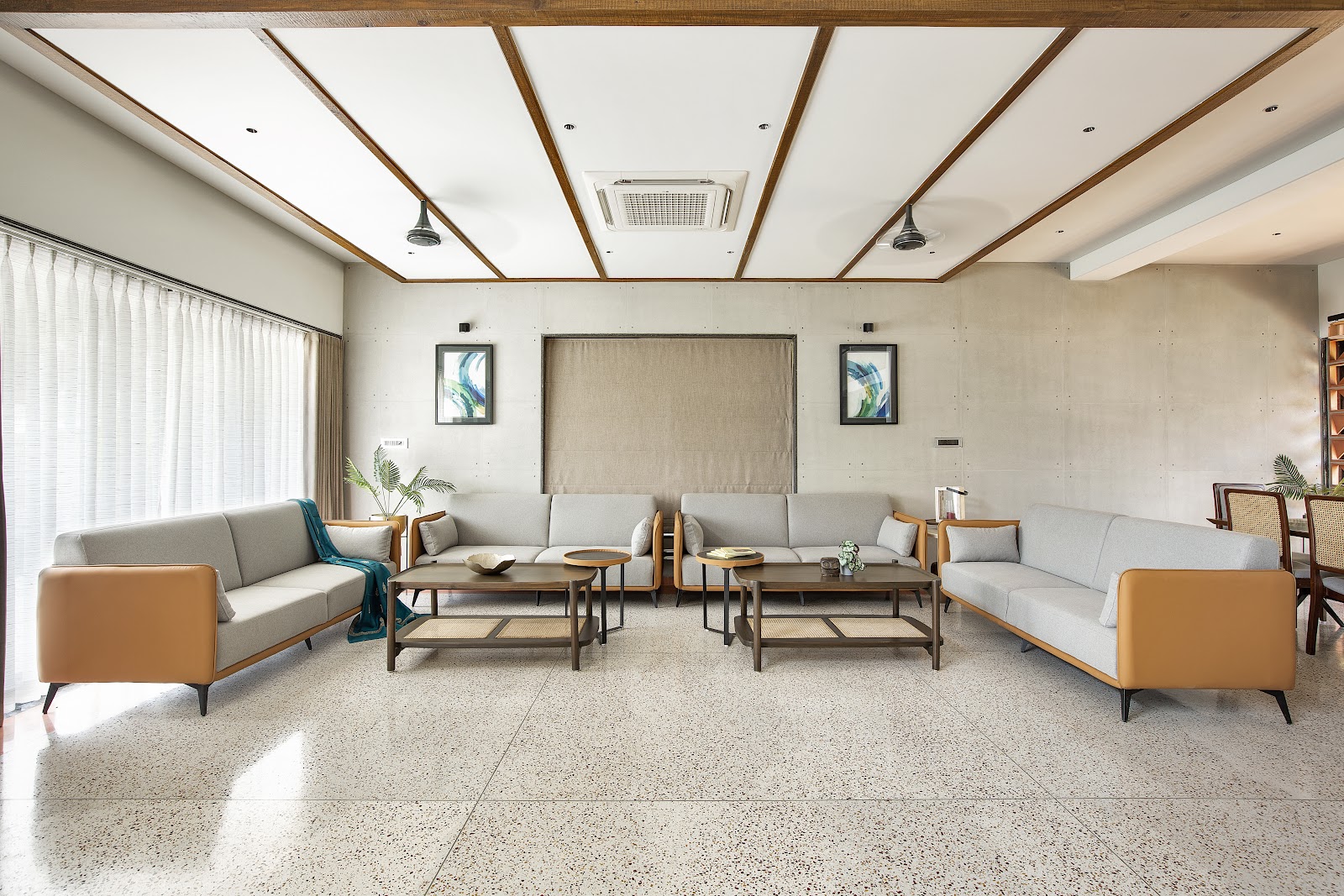 Real photo of a living room with speckled terrazzo flooring, an exposed concrete-panelled feature wall, a wood-beamed ceiling