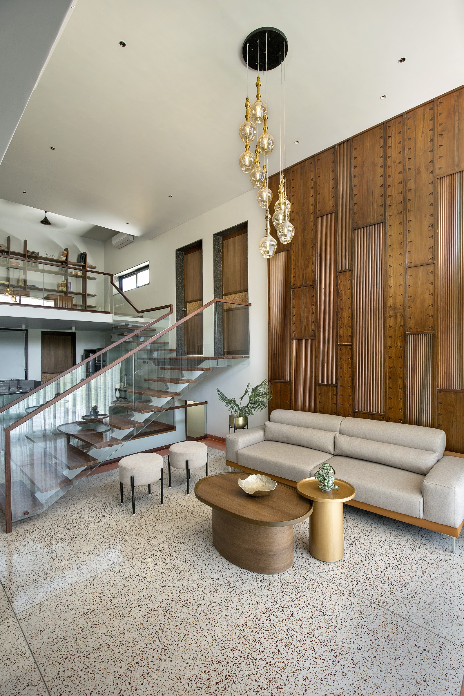 Double-height living room with a carved fluted wood feature wall, a cascading amber-glass pendant cluster, a terrazzo floor