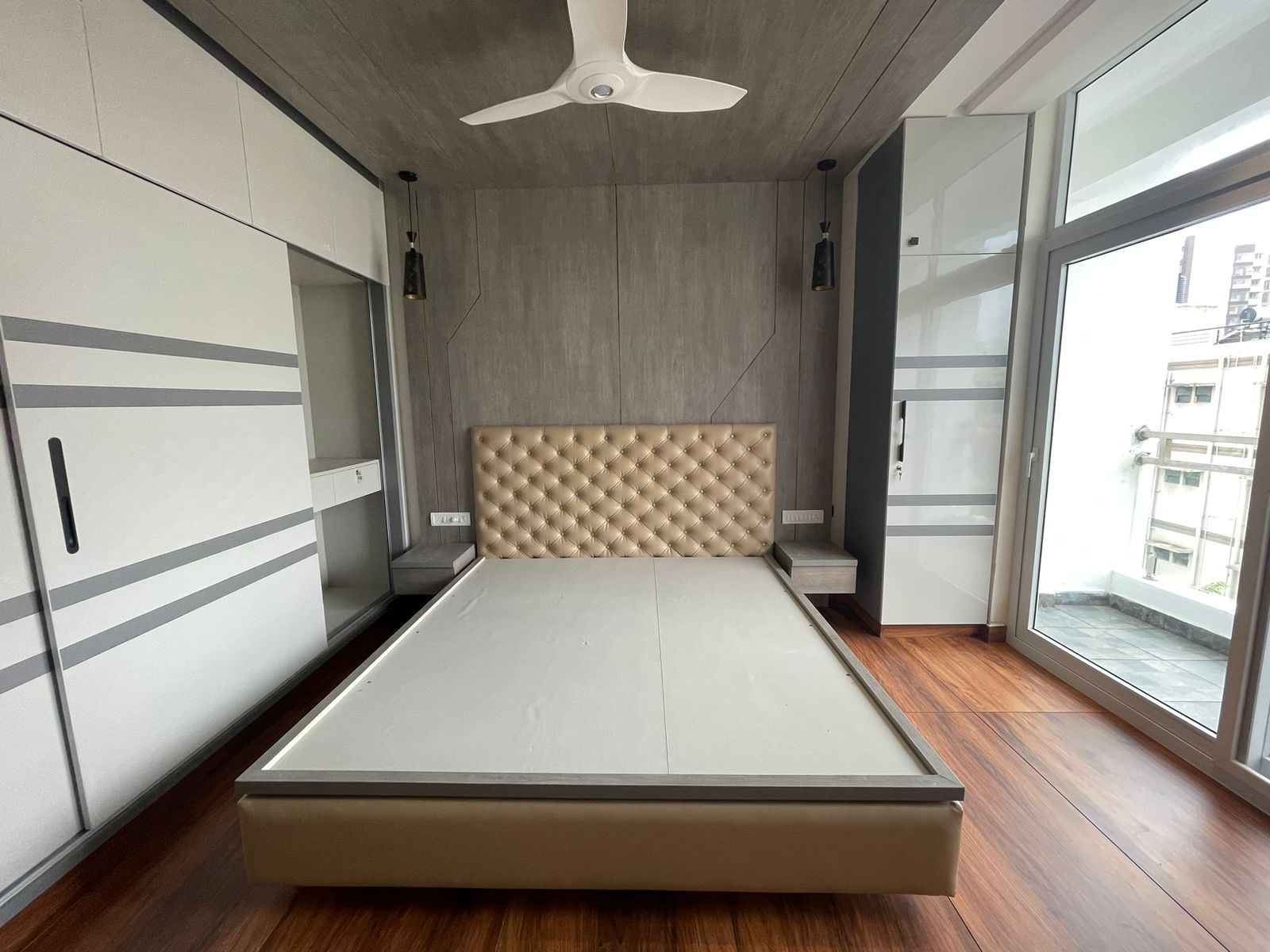 Master bedroom with a champagne tufted-leather bed and integrated grey floating nightstands under a geometric wood-panelled headboard wall