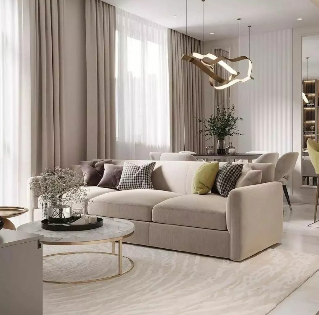 Living room with a beige textured sectional sofa styled with checkered and velvet cushions, a round marble-and-brass coffee table