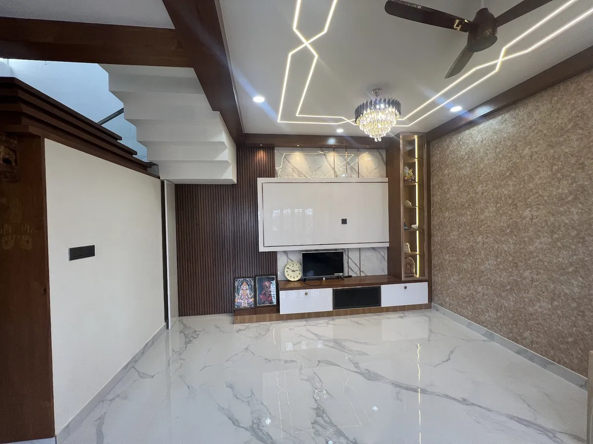 Unfurnished duplex hall with a fluted-walnut and marble TV wall, backlit display niches holding brass idols, a zig-zag linear LED pattern in the false ceiling