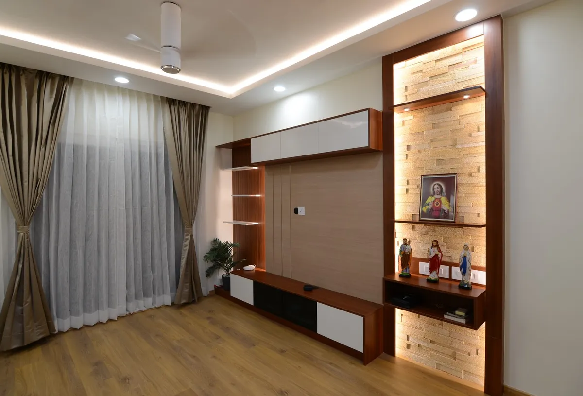 Living room TV wall in red-toned teak veneer with white gloss shutters, set beside a grazing-lit ledger-stone niche that holds a framed Sacred Heart picture