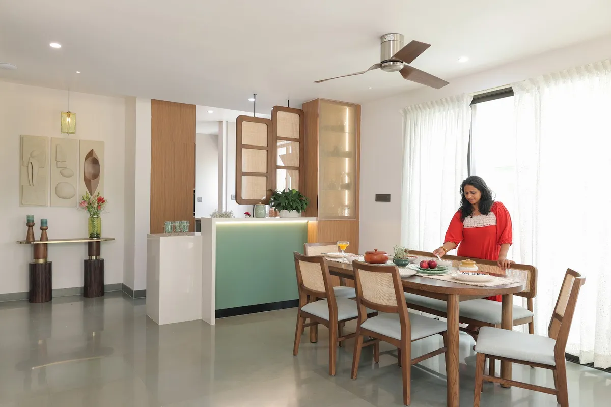 Dining area with a six-seater teak table and cane-back chairs, a cane-and-fluted-glass crockery tower next to a mint-green breakfast counter