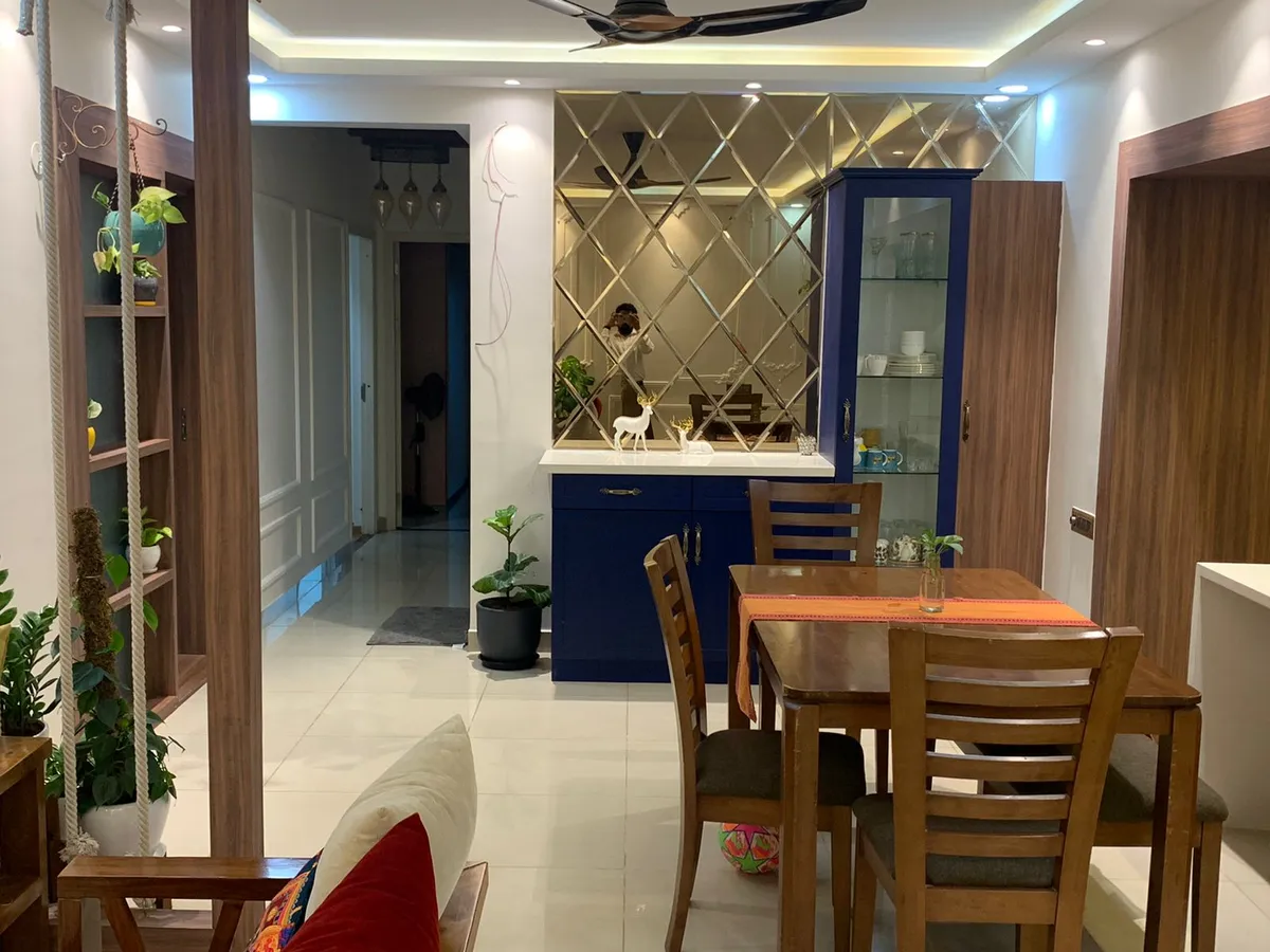 A dining nook with a wooden table set against a navy blue crockery cabinet topped with a diamond-mirror backsplash and deer figurine decor.