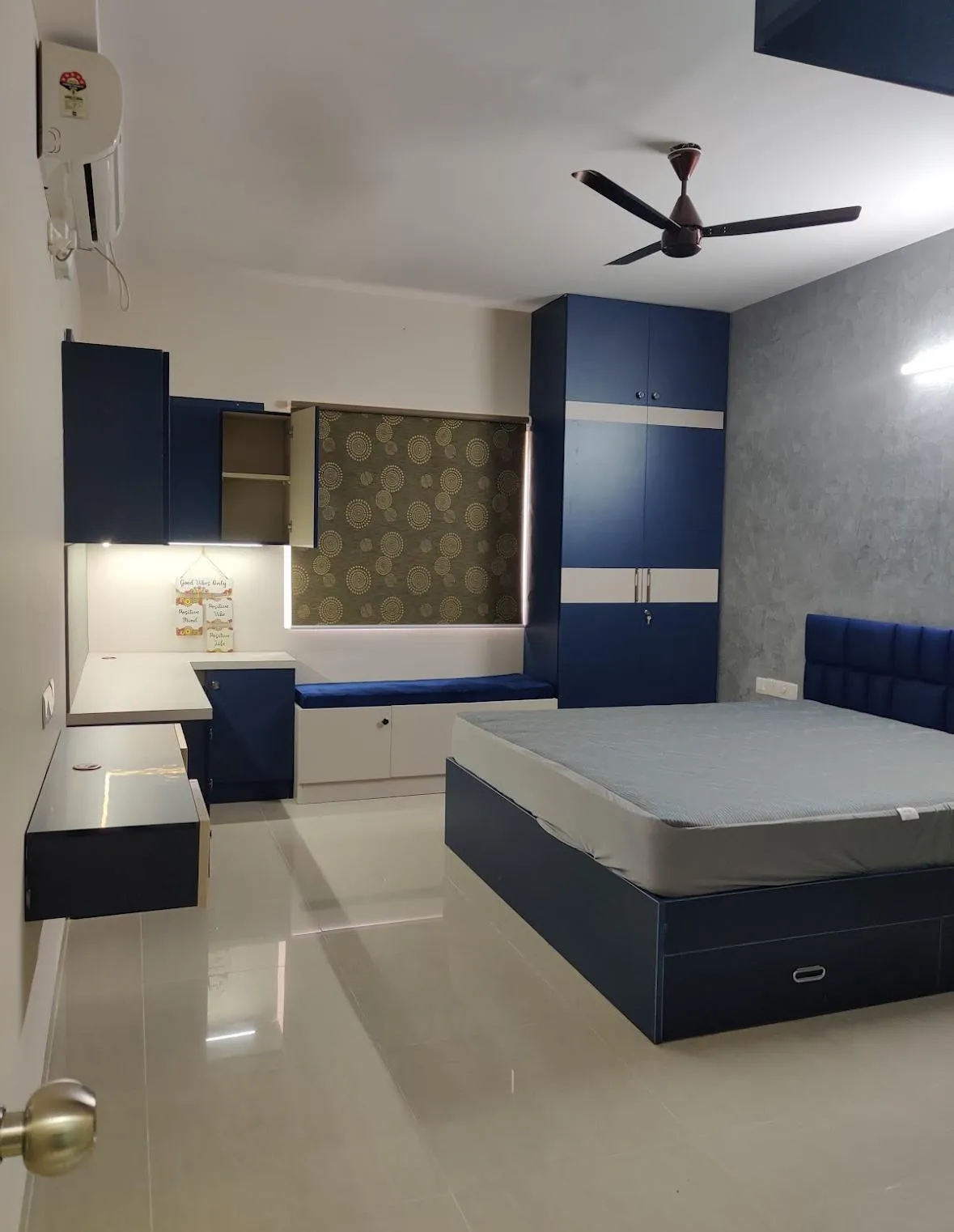 Navy laminate bedroom set — hydraulic storage bed with a channel-tufted blue velvet headboard against a grey textured wall, matching wardrobe