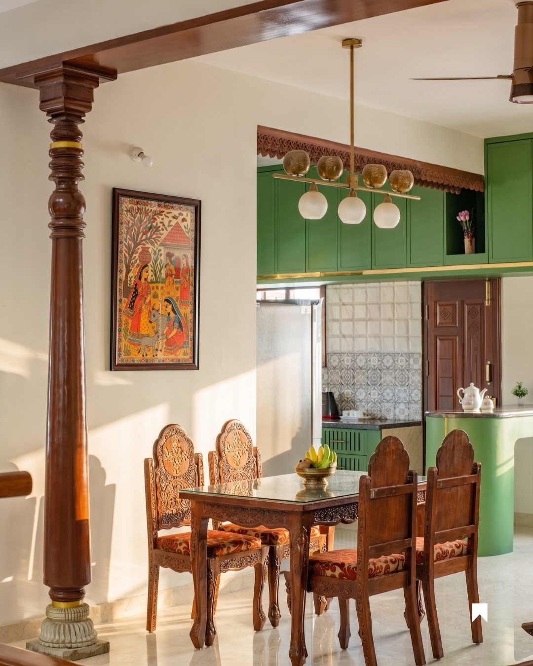Dining area with an intricately hand-carved wooden table and chairs beside a traditional turned wooden pillar, a folk-art painting on the wall