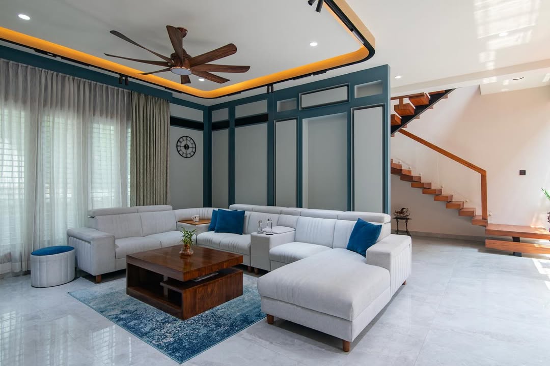Double-height living room with a teal moulded panel wall, cove-lit ceiling with a wood-blade fan, a light grey L-shaped sectional sofa