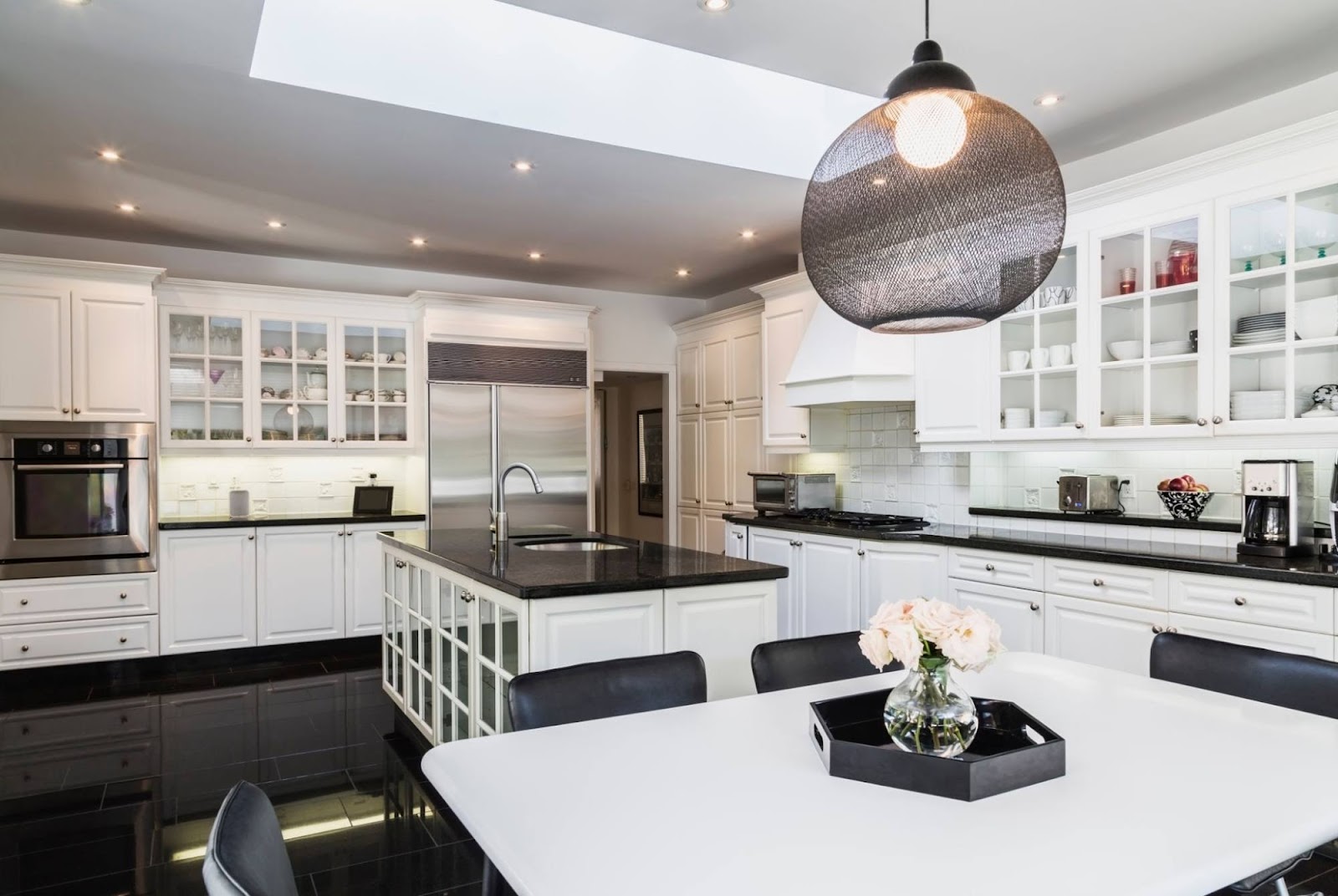 Open kitchen with white shaker cabinetry, a black granite island with glass-front lower panels, a large mesh-globe pendant light