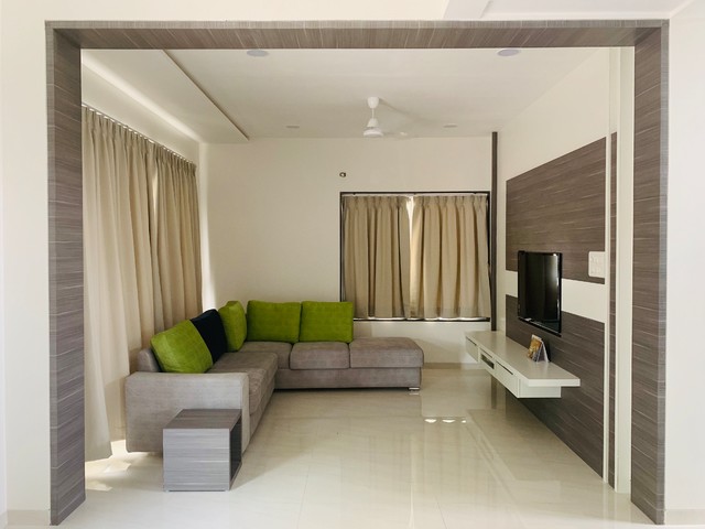 Living room framed by a wood-panelled archway, with a grey L-shaped sofa in olive cushions facing a wall-mounted TV on a laminate feature wall.