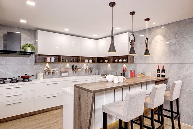 Kitchen with a white gloss L-shaped run and a central island breakfast bar topped in wood, three black pendant lights above, grey stone-effect walls