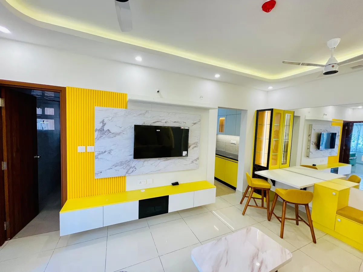 Open-plan living-dining space with a marble-panel TV wall accented by yellow fluted panelling, a yellow-and-white dining nook with bar stools