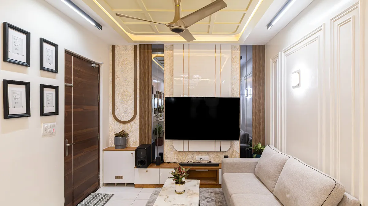Photograph of a compact living room whose TV wall combines damask wallpaper, fluted wood, mirror strips and gold inlay lines