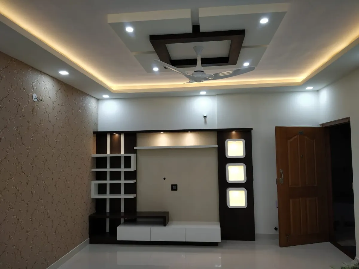 Living room feature wall with a stepped pop false ceiling and cove lighting over a dark-wood TV unit with backlit display niches and floral wallpaper alongside
