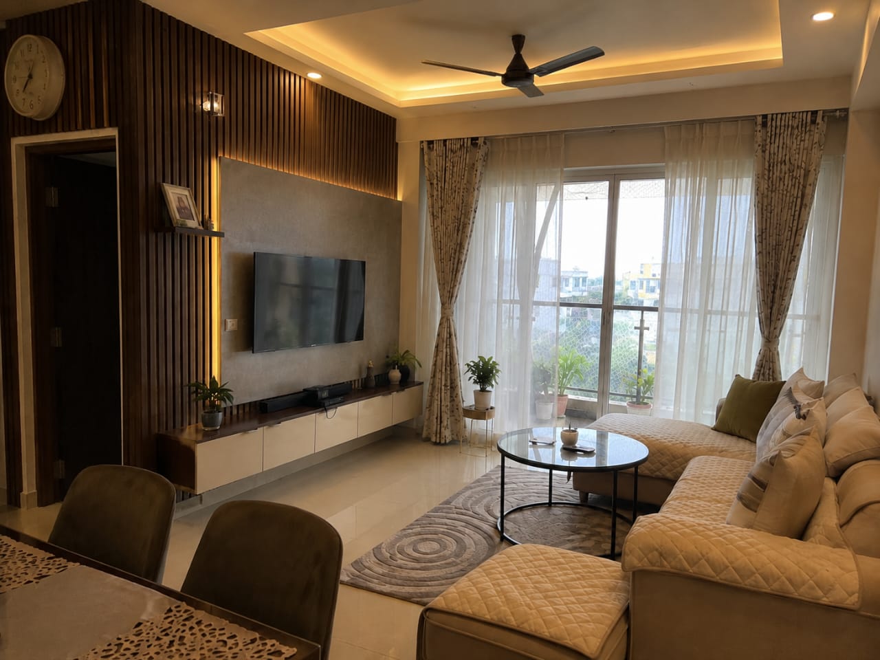Living room with a backlit wood-fluted TV wall, a floating console below, a beige quilted L-shaped sectional sofa around a round marble-top coffee table on a