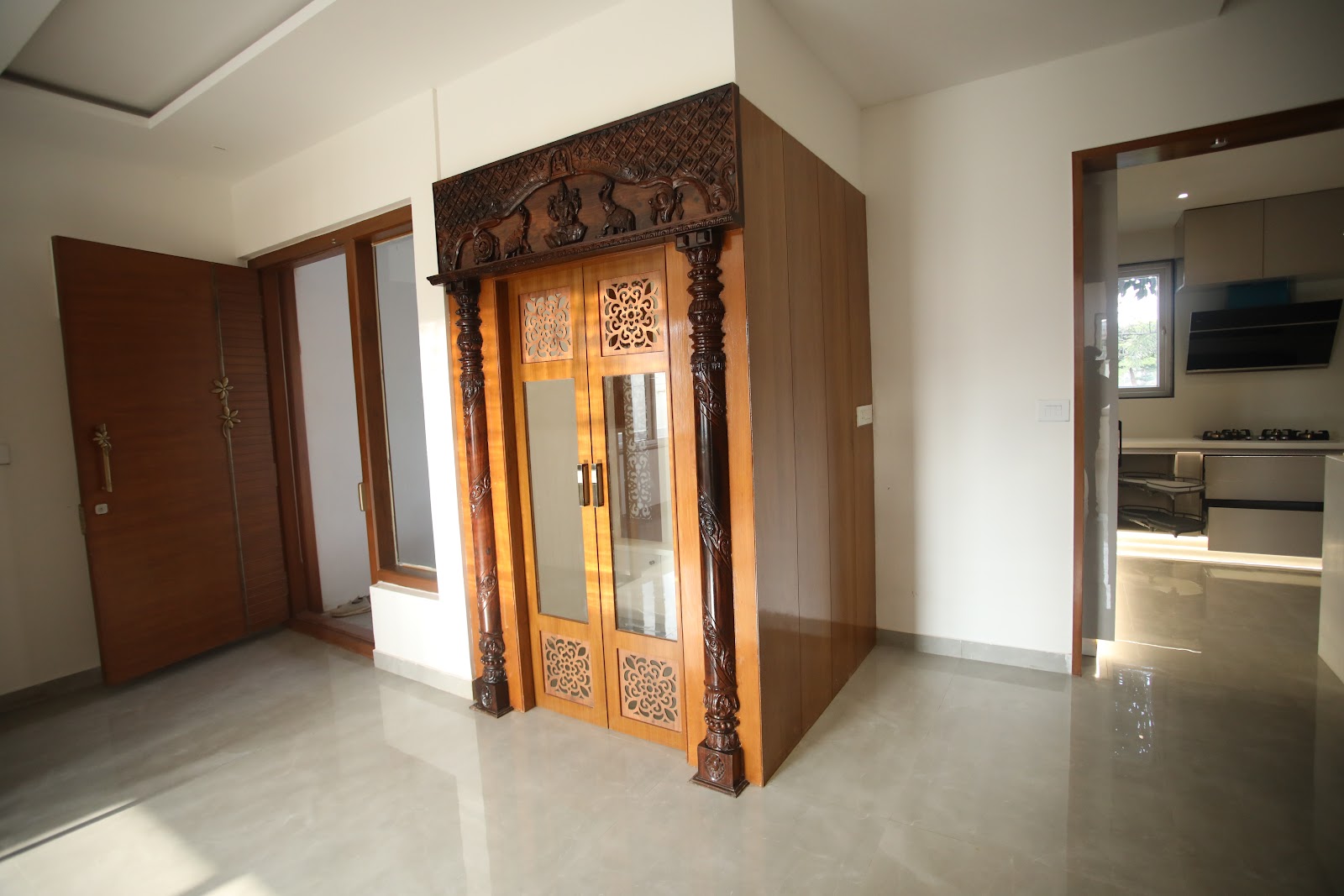 Free-standing pooja room enclosure in the entry foyer with hand-carved traditional wooden doors, pillared surround, and a floral fretwork transom