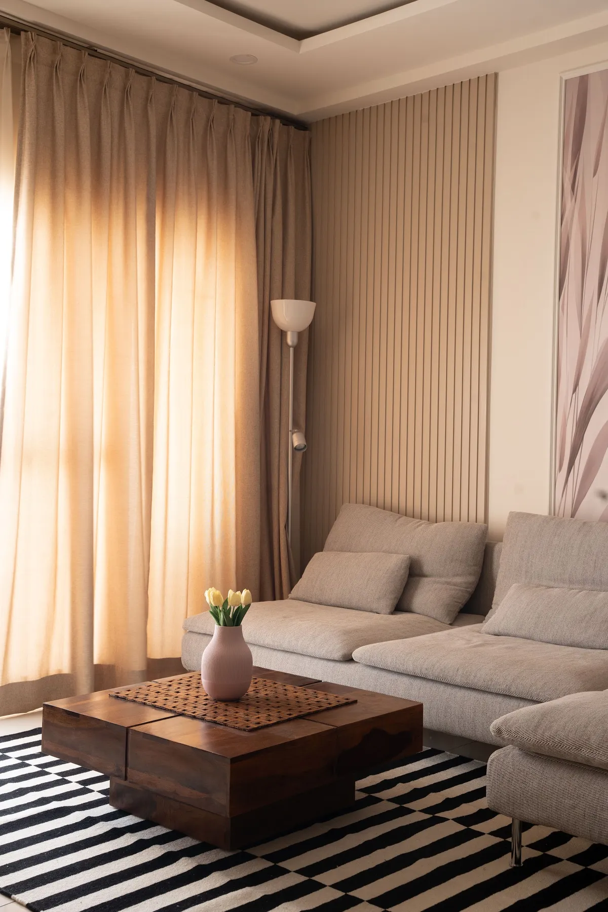 Living room corner with fluted wall panelling, a beige upholstered sectional sofa, a striped rug, and a solid-wood block coffee table.