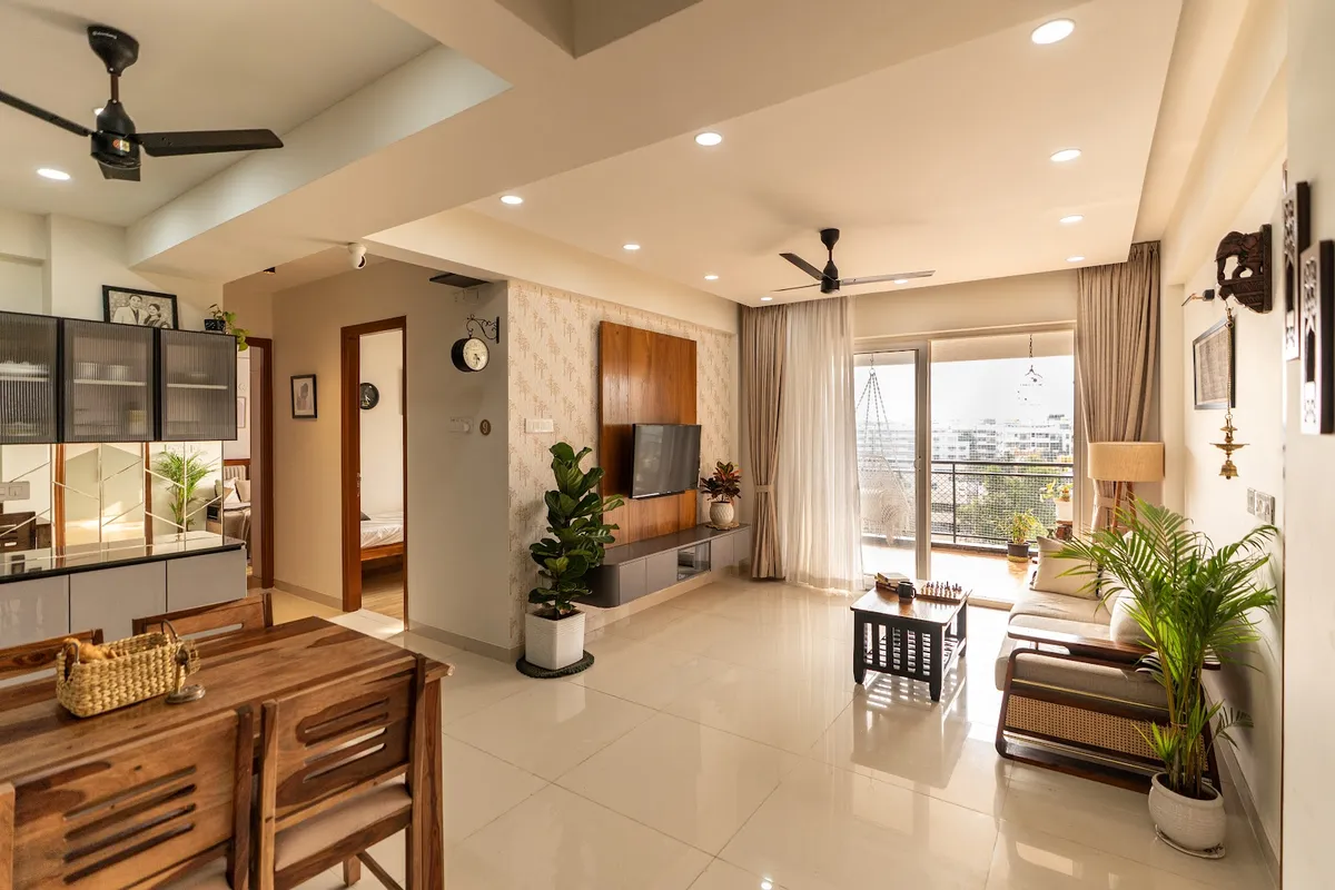 Open-plan apartment interior combining a wood dining table with woven basket, a living area with a wood-toned TV wall and beige sofa