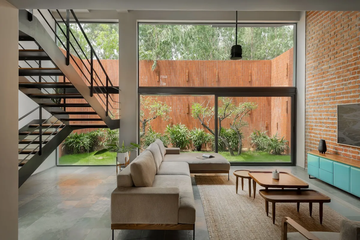 Double-height living room with an open-riser steel-and-timber stair, an exposed brick wall carrying the TV above a turquoise sideboard