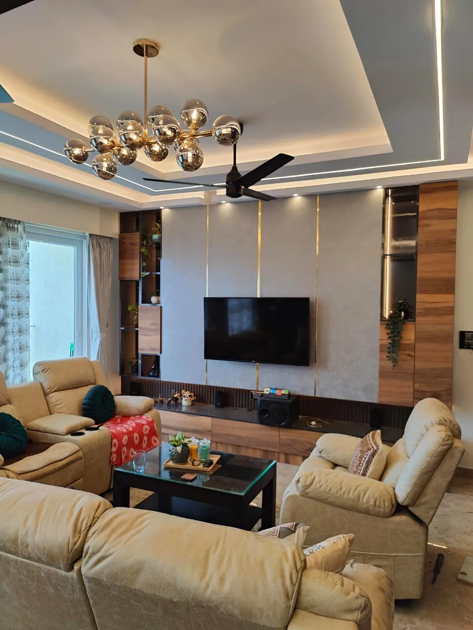 Beige leather recliner set around a black-and-glass coffee table faces a grey textured TV wall inlaid with vertical brass strips