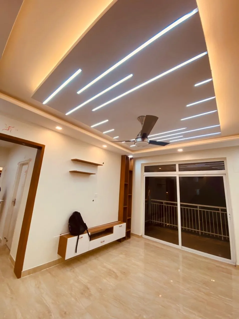 Empty living room at handover under a taupe false ceiling fanned with slim linear LED profiles