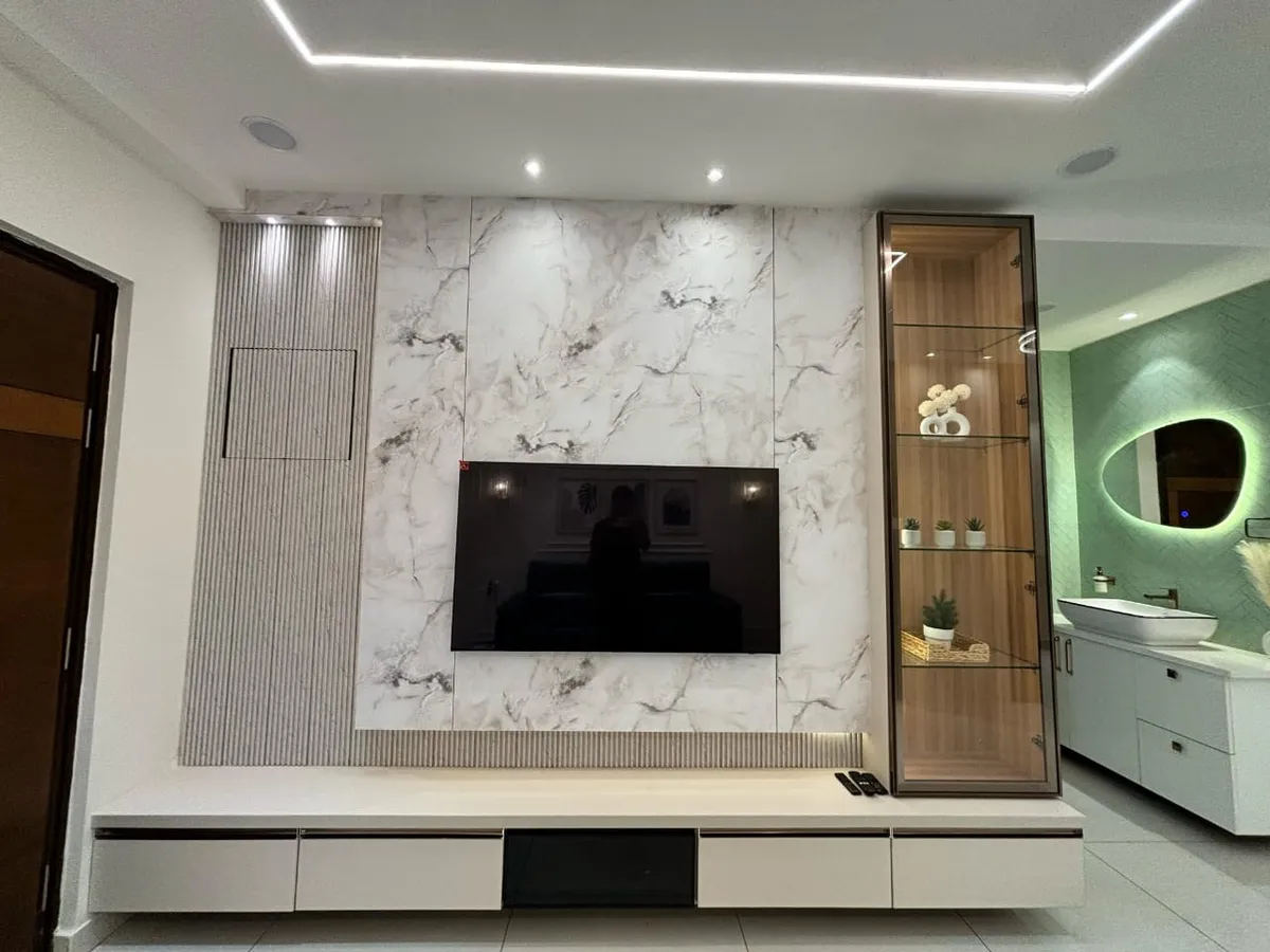 Living room TV wall clad in book-matched white marble with a fluted side panel and a backlit glass display cabinet, floating console below