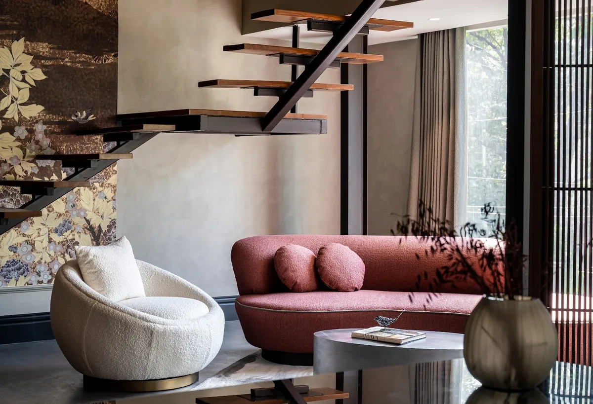 Living room beneath a floating black-steel staircase with wood treads, featuring a curved terracotta boucle sofa, a round cream boucle armchair