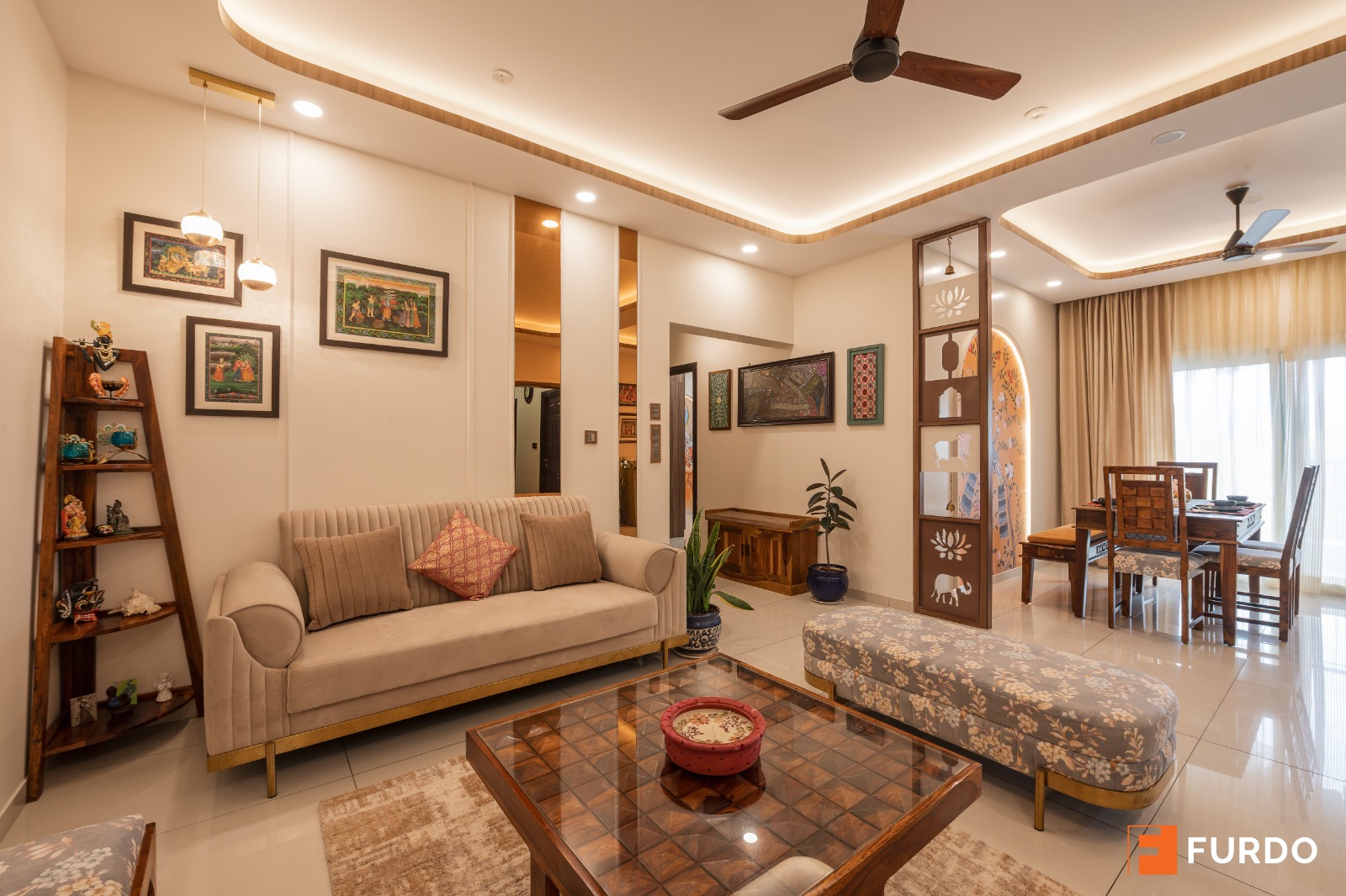 Living room with a beige channel-tufted sofa and a wood coffee table, facing a carved jaali partition with lotus and elephant motifs that screens the dining