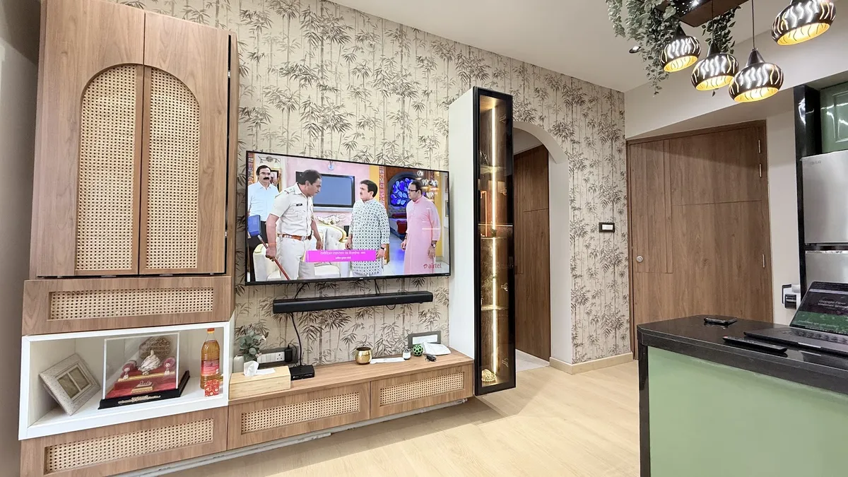 Living room TV wall with a cane-front storage unit, bamboo-leaf wallpaper backdrop, and a backlit glass display nook beside an archway toward the kitchen.