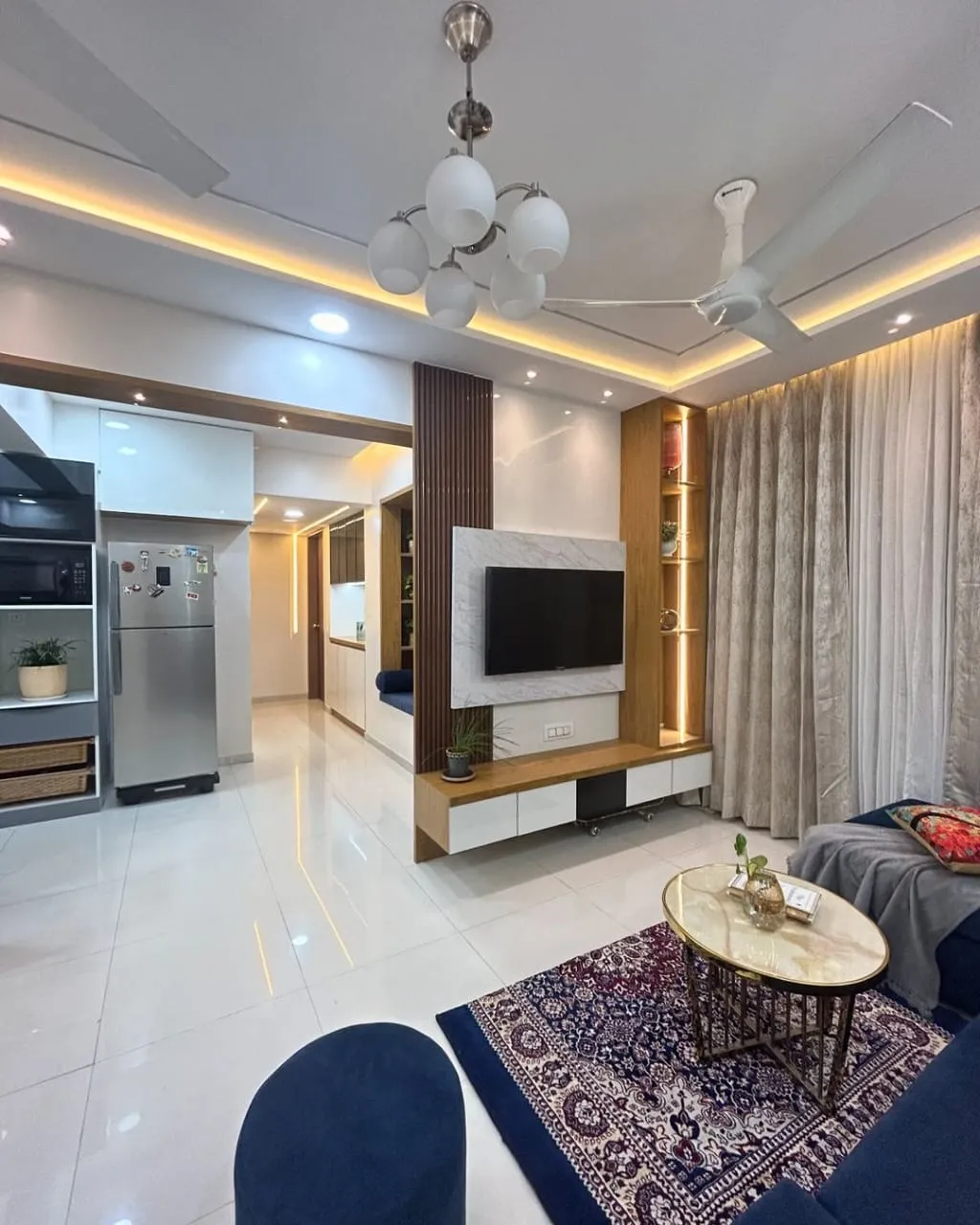 Living room with a marble-clad TV unit flanked by a fluted wood pillar and open display shelving, a navy sofa