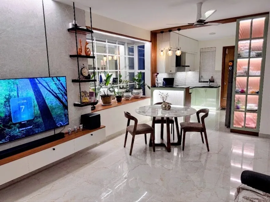 Open-plan floor seen end to end: a grey stone-clad TV wall with black metal floating shelves, a round marble-top dining table in the middle