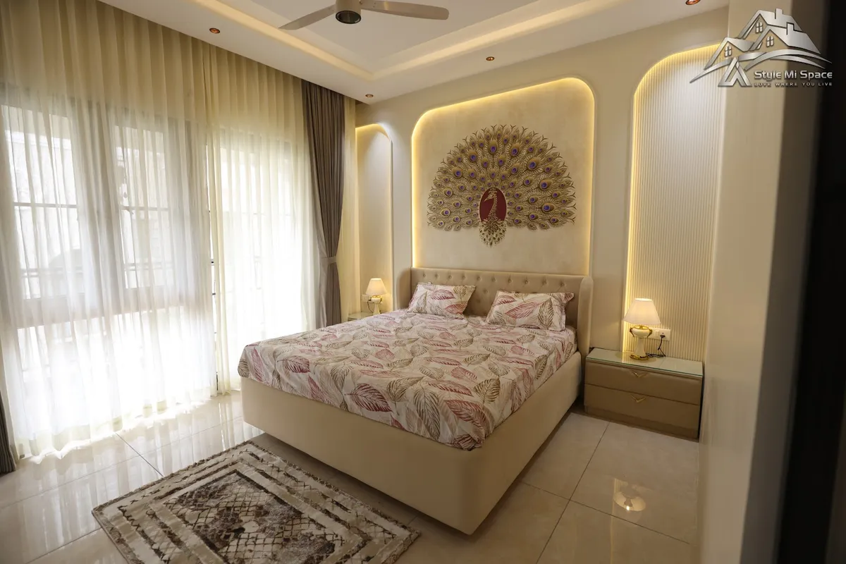 Cream bedroom where a buttoned upholstered bed sits in a backlit arched niche carrying a gold-and-purple metal peacock relief