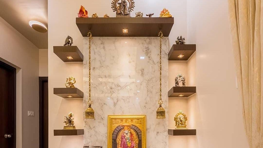 Wall-mounted pooja shrine with a book-matched marble backing panel, a golden deity frame, hanging brass bells