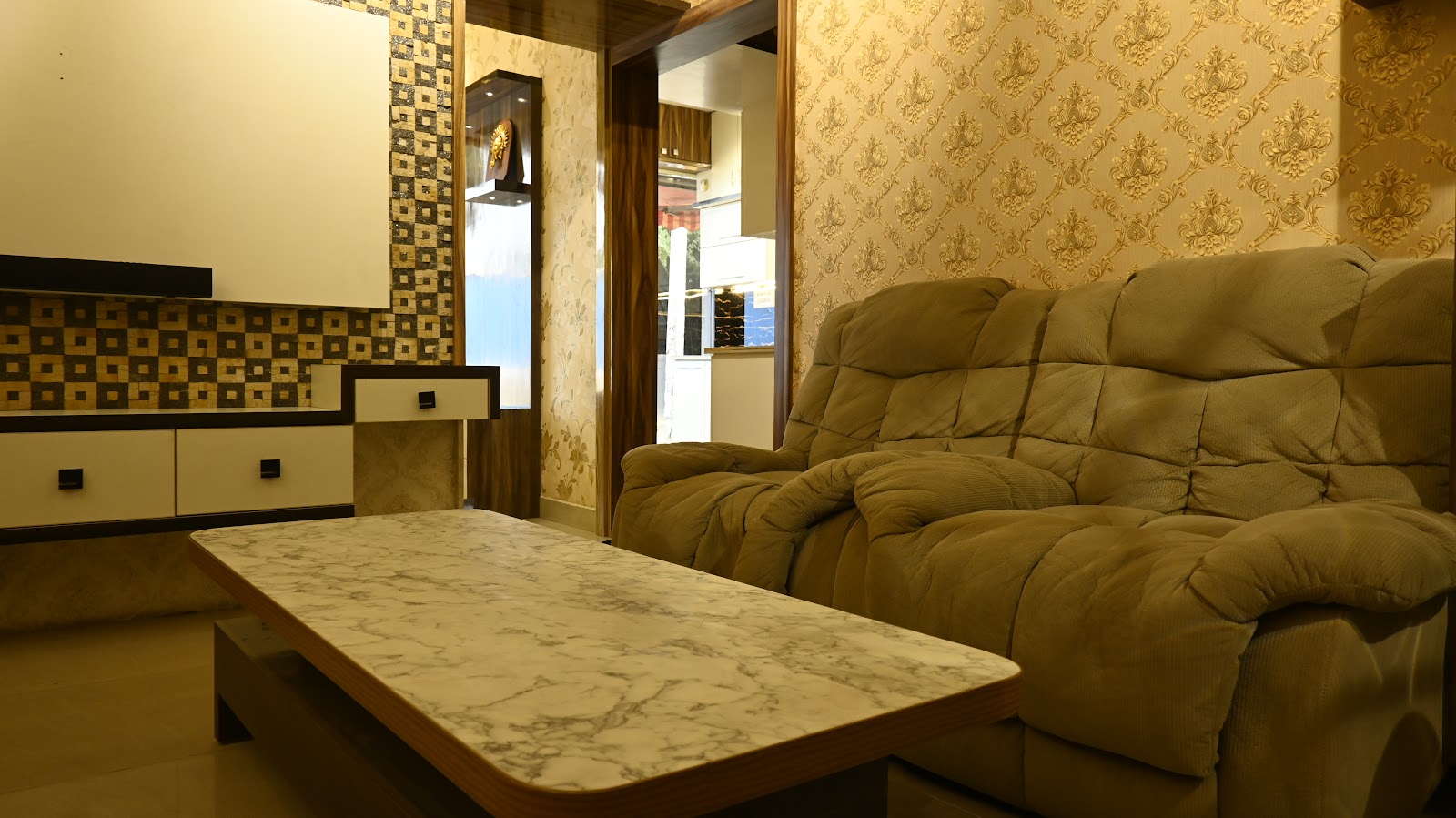 Living room with gold damask wallpaper, a tufted olive recliner sofa and a marble-top coffee table facing a checkered-tile TV console wall with a lit display