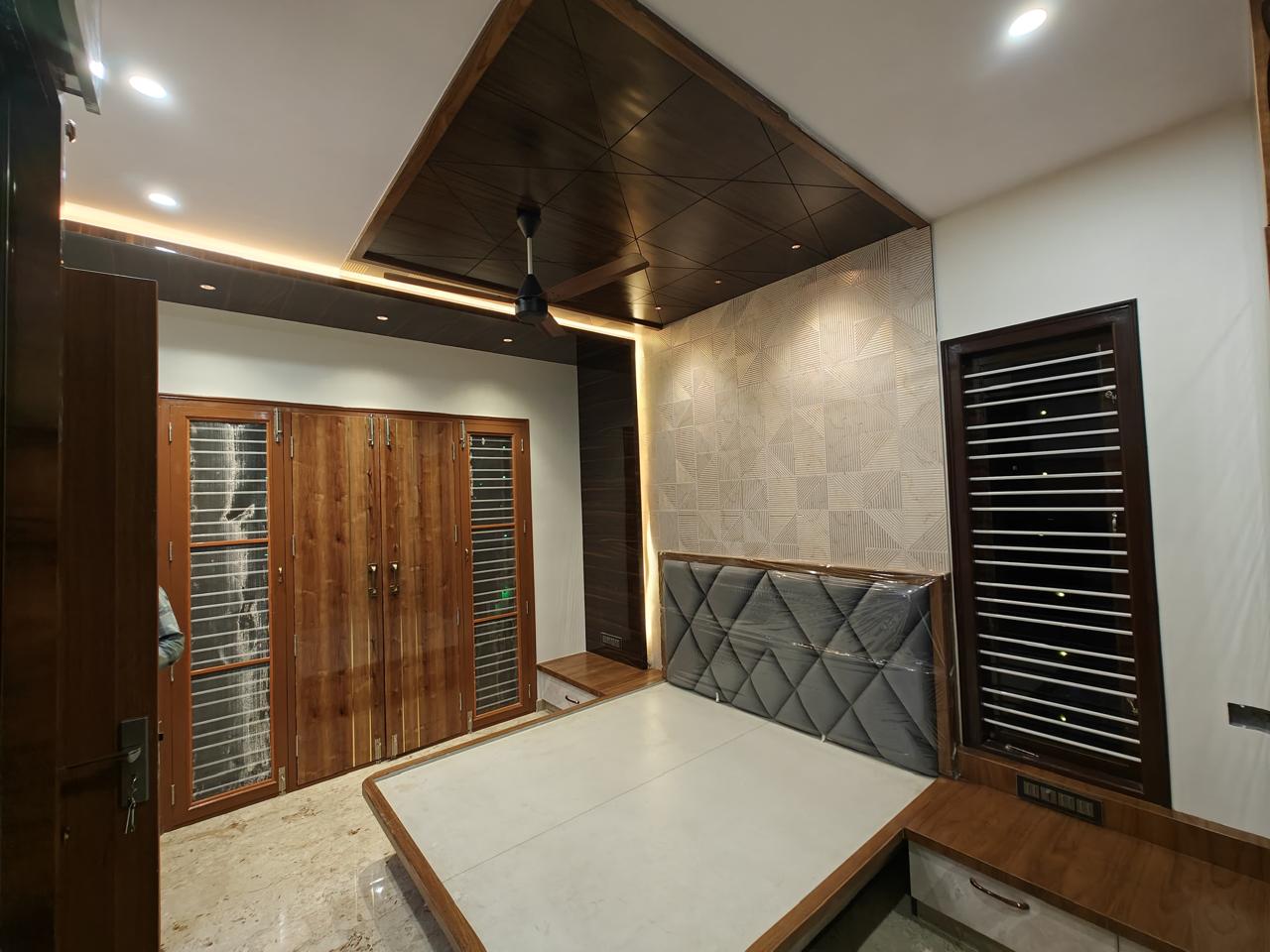 Bedroom with an angled wood-panel ceiling in a diamond lattice pattern, cove lighting, a grey diamond-tufted headboard still wrapped in protective plastic