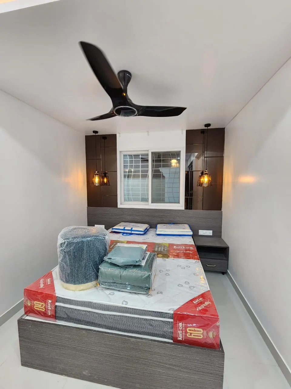 Compact bedroom with a grey upholstered-look headboard wall, dark wood side panels with cage pendant lights