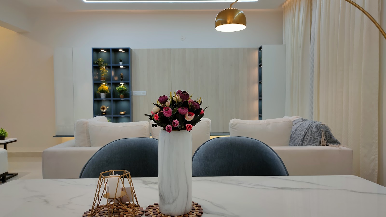 Dining nook with a white marble table, curved blue velvet chairs, and a gold dome pendant light, opening into the living room beyond.