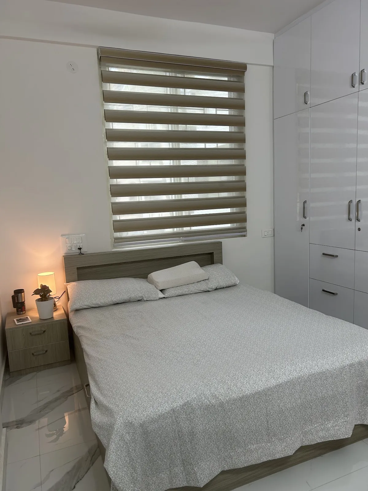 Compact bedroom with a light-oak laminate bed and matching two-drawer nightstand set under a beige zebra blind