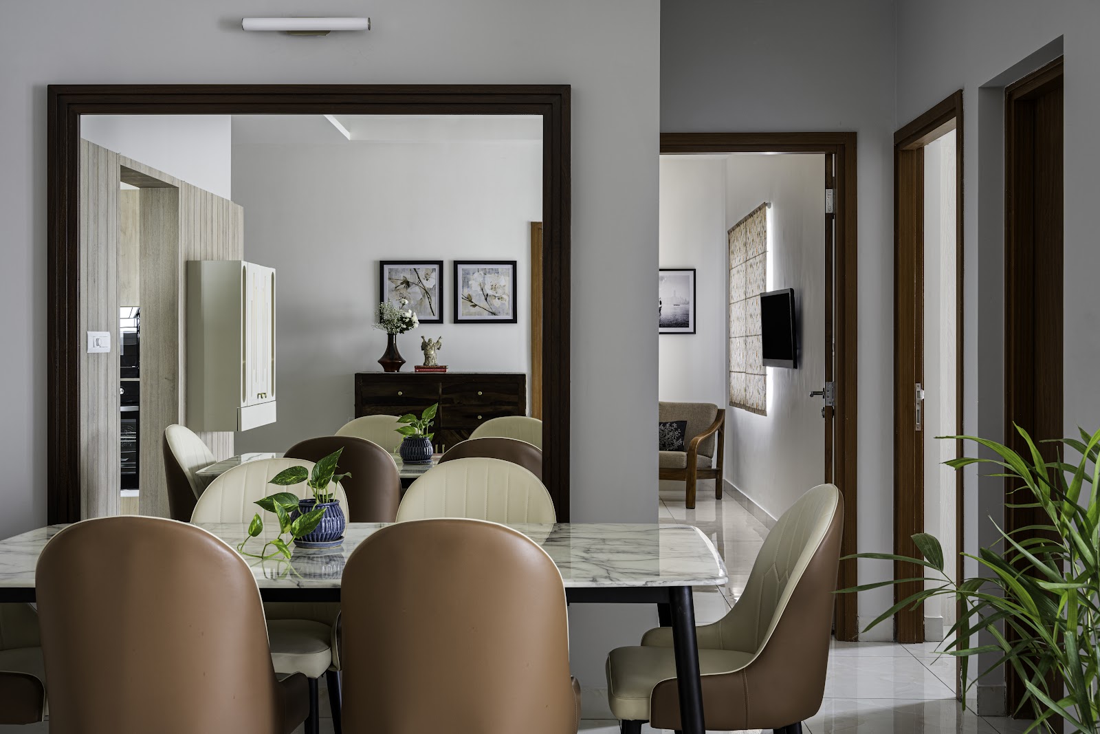 A dining room with a marble-top table and tan leather chairs reflected in a large wall mirror, a dark wood console with framed art beyond